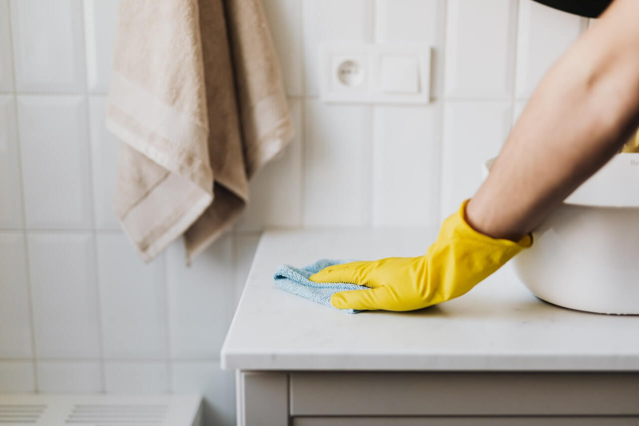 una mano con guanto pulise lavandino come parte dei servizi negli appartamenti per studenti di Student living